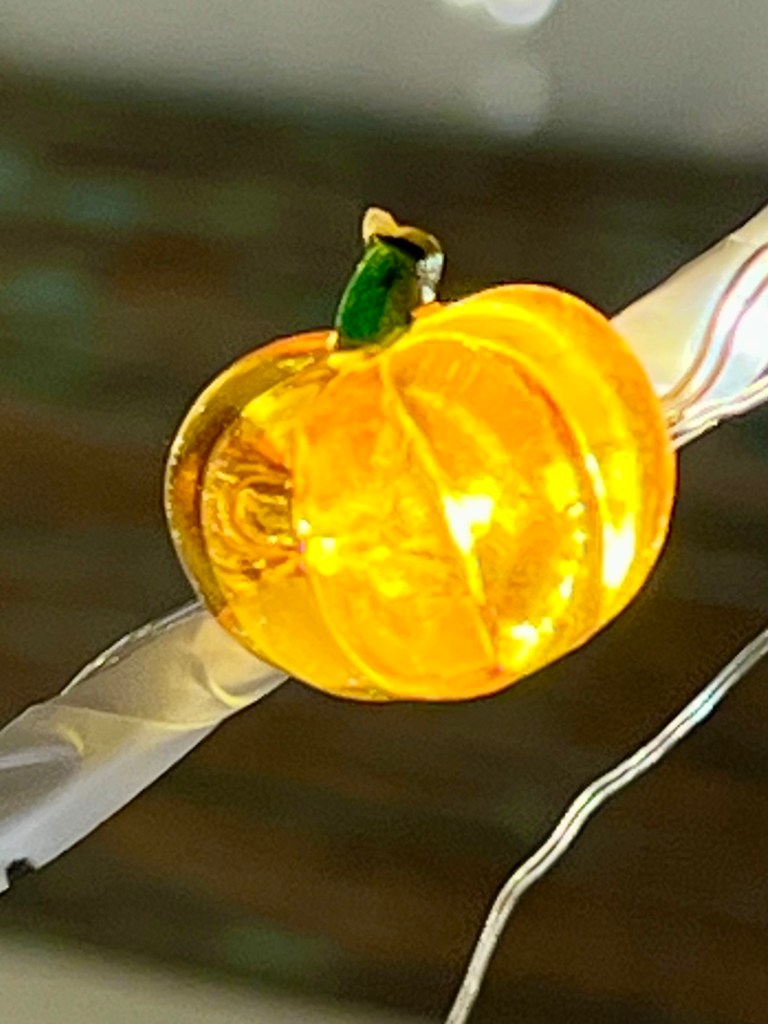 Close-up of a decorative yellow pumpkin light, emphasizing its bright color and detail, hanging on a string of lights.