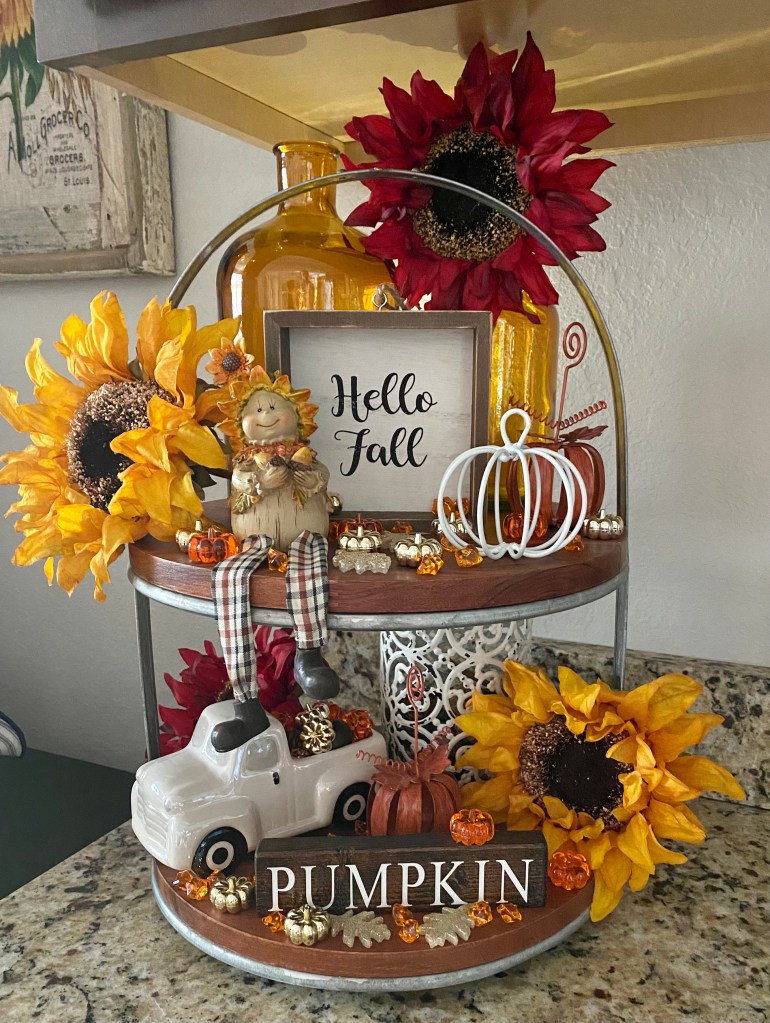 A cozy fall decoration featuring sunflowers, a whimsical figure, a pumpkin, and a small white truck, along with a sign that says 'Hello Fall'.